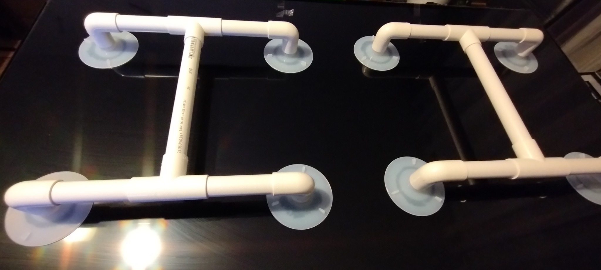 Dwa uchwyty z rur PCV z przyssawkami na błyszczącej czarnej powierzchni, prawdopodobnie do mocowania tymczasowych elementów.