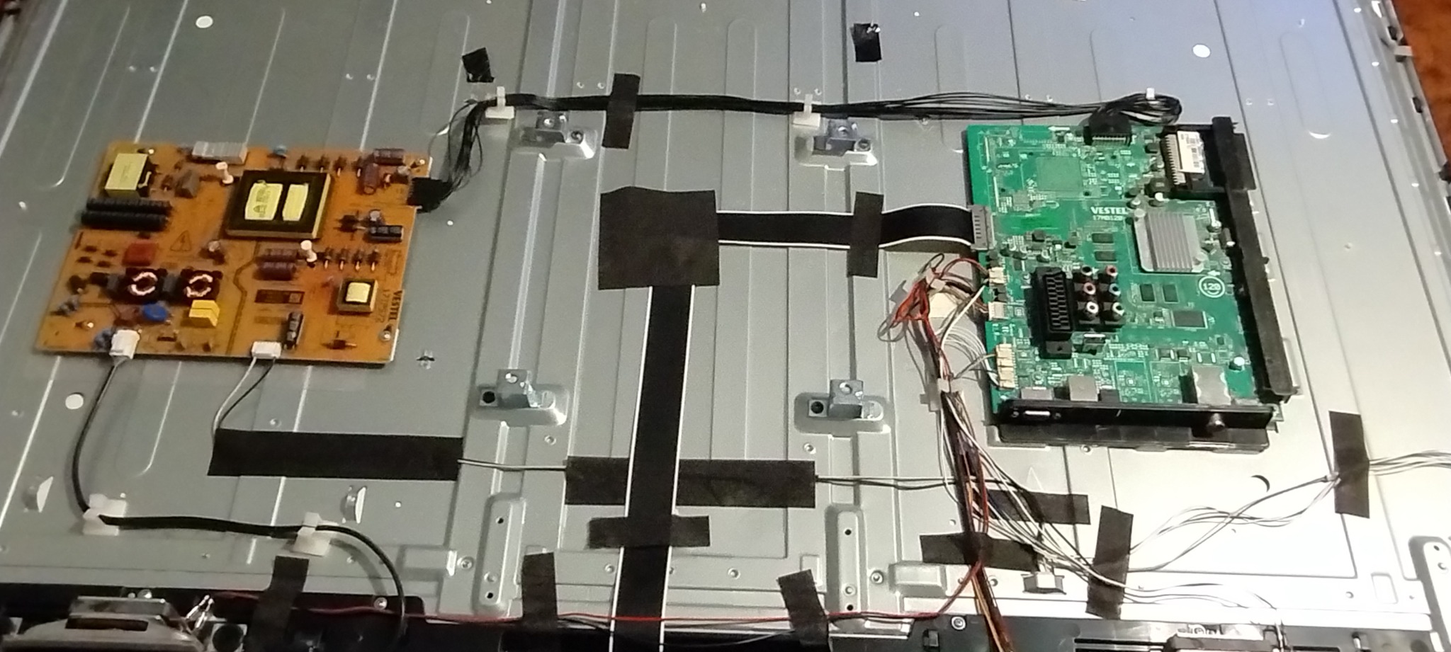 Wnętrze telewizora z widocznymi płytkami drukowanymi, przewodami i taśmą izolacyjną