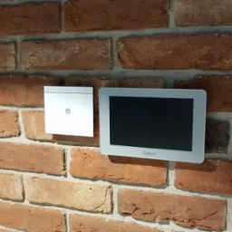 Panel sterowania alarmem i czujnik ruchu zamontowane na ścianie z czerwonej cegły.