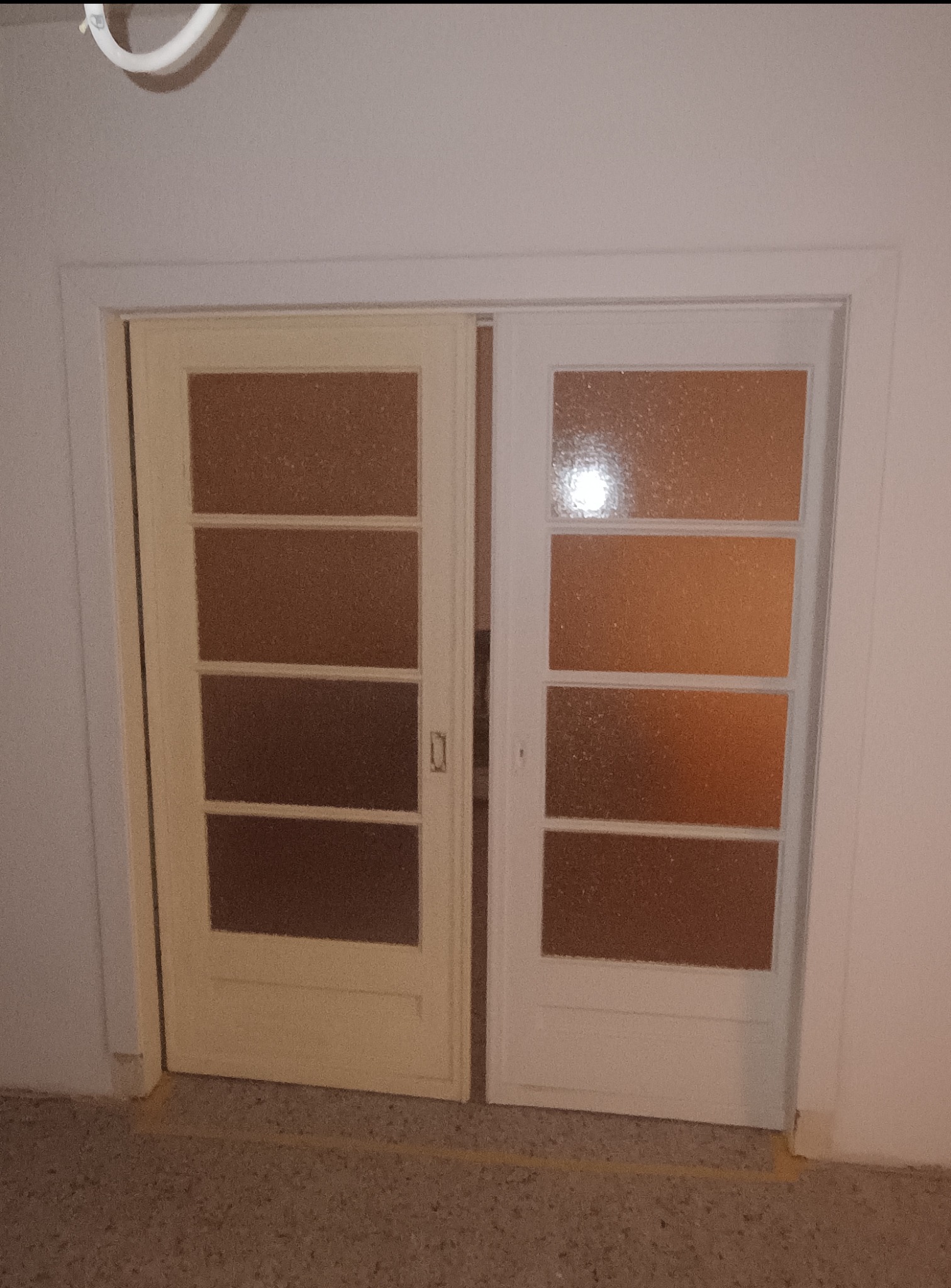 Para drzwi przesuwnych z czterema szybkami z matowego szkła, jedna pomalowana na biało, druga na kremowo, zamontowane w białej futrynie.