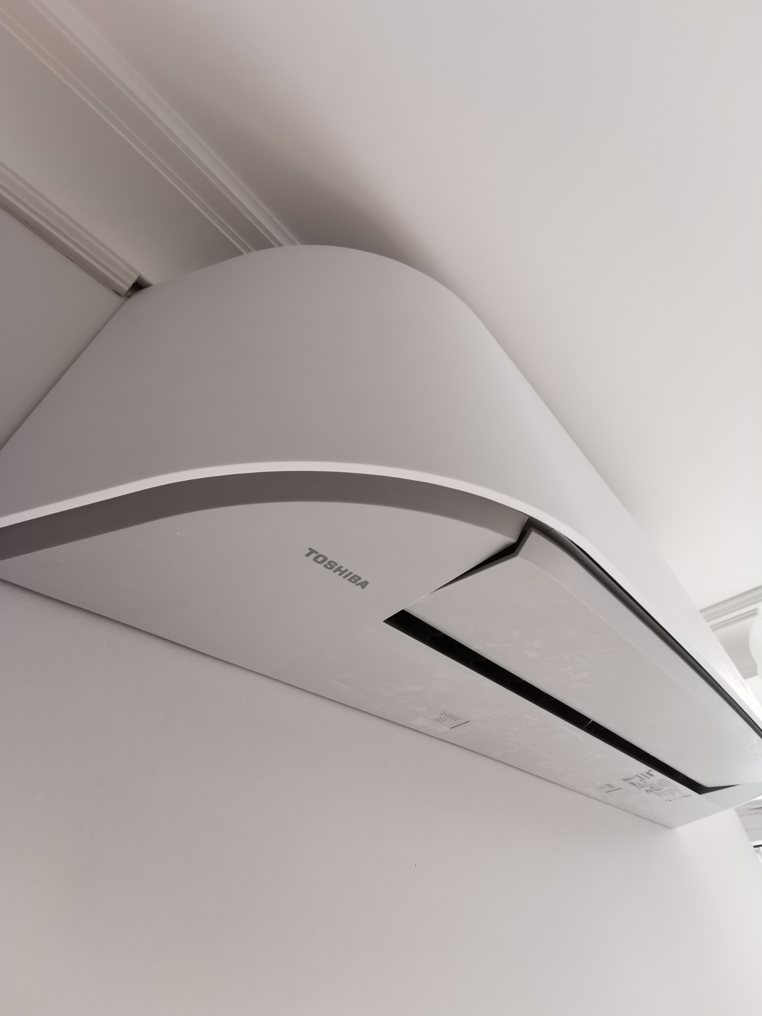 Nowoczesny, biały klimatyzator Toshiba zamontowany na ścianie, widoczne detale obudowy i logo producenta, eleganckie wykończenie sufitu w tle.