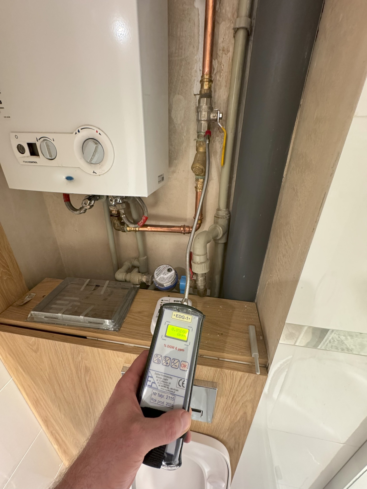 Miernik gazu przy kotle gazowym podczas próby szczelności instalacji, widoczny wyświetlacz z odczytem, elementy instalacji gazowej z rurami miedzianymi.