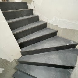 Rafal Chabiniak - Wykończone schody z szarych płytek, widoczne ślady prac wykończeniowych na ścianach. Ujęcie z dołu, podkreślające geometrię stopni.