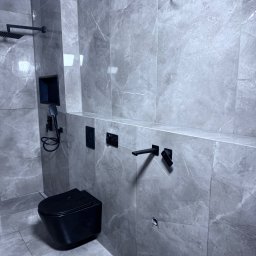 Rafal Chabiniak - Nowoczesna łazienka w szarościach z czarną armaturą: wisząca toaleta, deszczownica, bateria umywalkowa. Minimalistyczny design, marmurowe płytki, oświetlenie punktowe.
