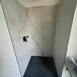 Rafal Chabiniak - Nowoczesna kabina prysznicowa walk-in z czarną armaturą i marmurowymi płytami w Wymiarkach. Minimalistyczny design z odpływem liniowym i deszczownicą.