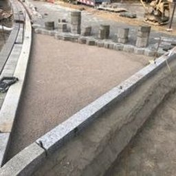 Przygotowanie podłoża z piasku i obrzeży z kostki granitowej na posesji. Widoczne ułożone krawężniki i palisady z granitu. Częściowo gotowy teren pod przyszłą nawierzchnię.