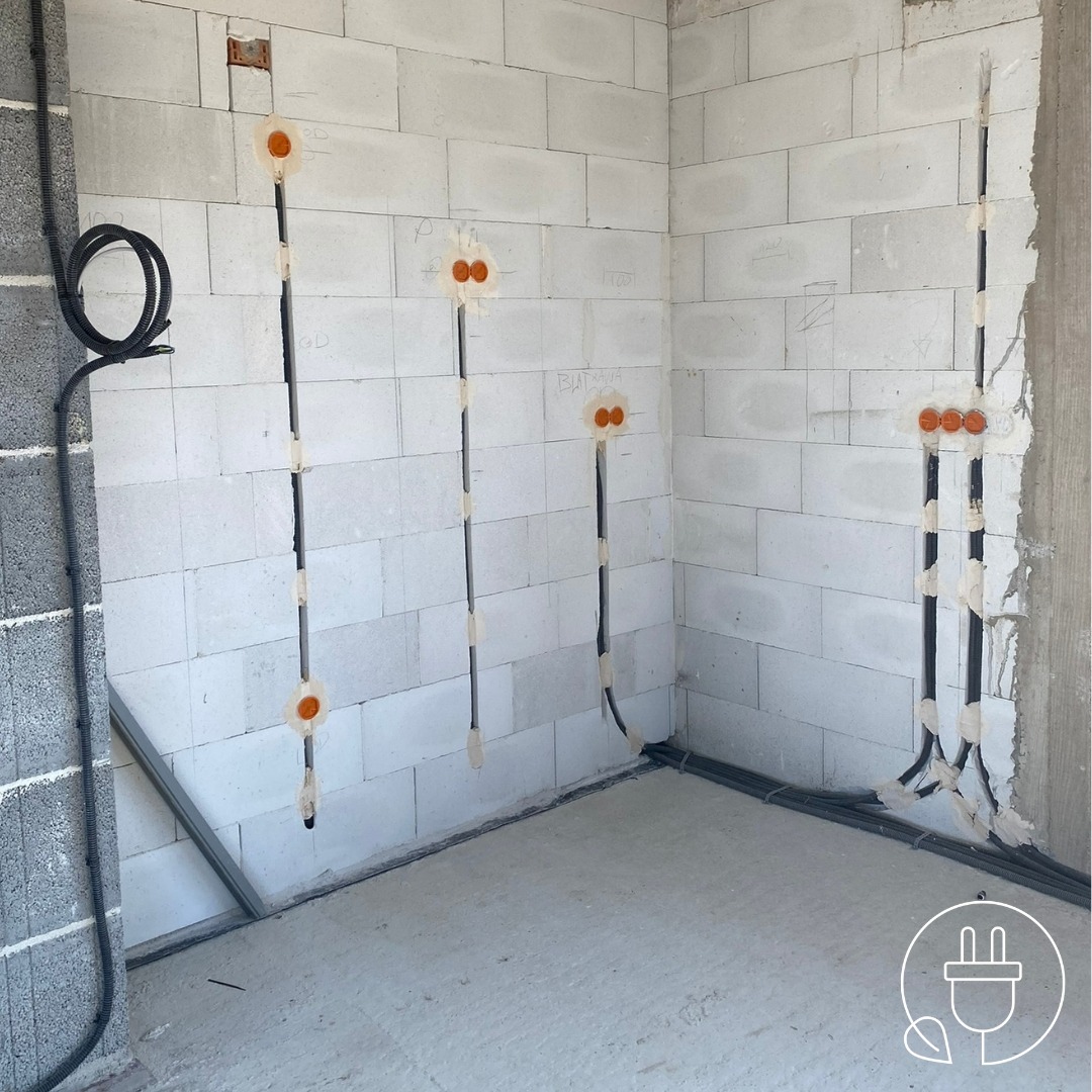 Wnętrze w trakcie prac elektrycznych: w ścianach z betonu komórkowego poprowadzone kable, widoczne puszki instalacyjne. Czarny kabel biegnie wzdłuż ściany.