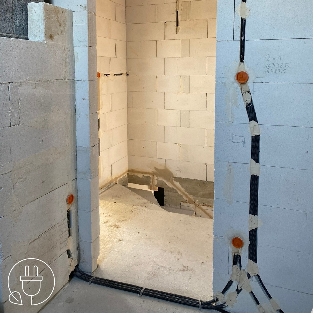 Wnętrze w trakcie prac elektrycznych: kable w peszlach, pomarańczowe puszki podtynkowe na ścianach z betonu komórkowego. Widoczne przygotowania do instalacji elektrycznej.