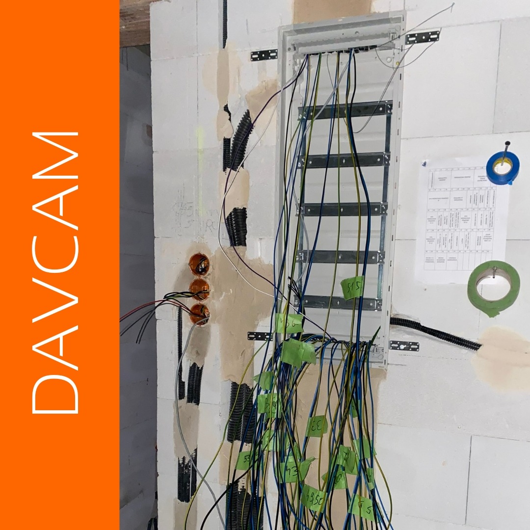 Rozdzielnia elektryczna w trakcie montażu w surowym wnętrzu. Widoczne kable, puszki instalacyjne i schemat. Oznakowane przewody z użyciem taśmy. Ściany z betonu komórkowego.