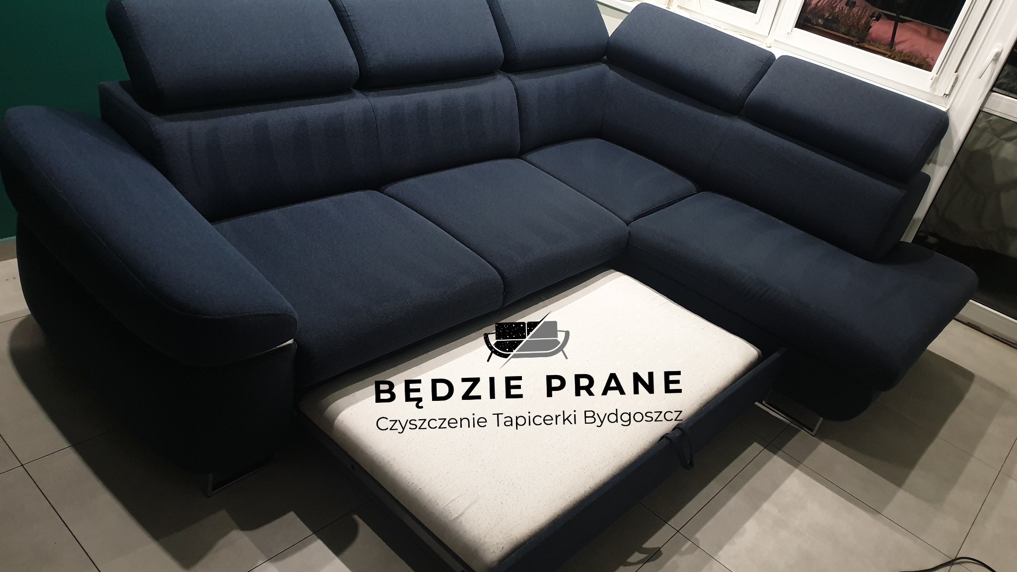 Narożnik z ciemnoniebieską tapicerką, z wysuniętą częścią z jasną tapicerką, na której widnieje napis 'Będzie Prane Czyszczenie Tapicerki Bydgoszcz' z logo firmy.