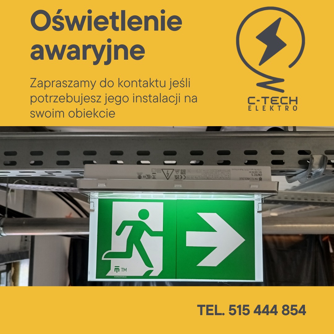 Zamontowany znak ewakuacyjny z podświetleniem LED, umieszczony pod sufitem, widoczne elementy instalacji elektrycznej i metalowa konstrukcja mocująca.