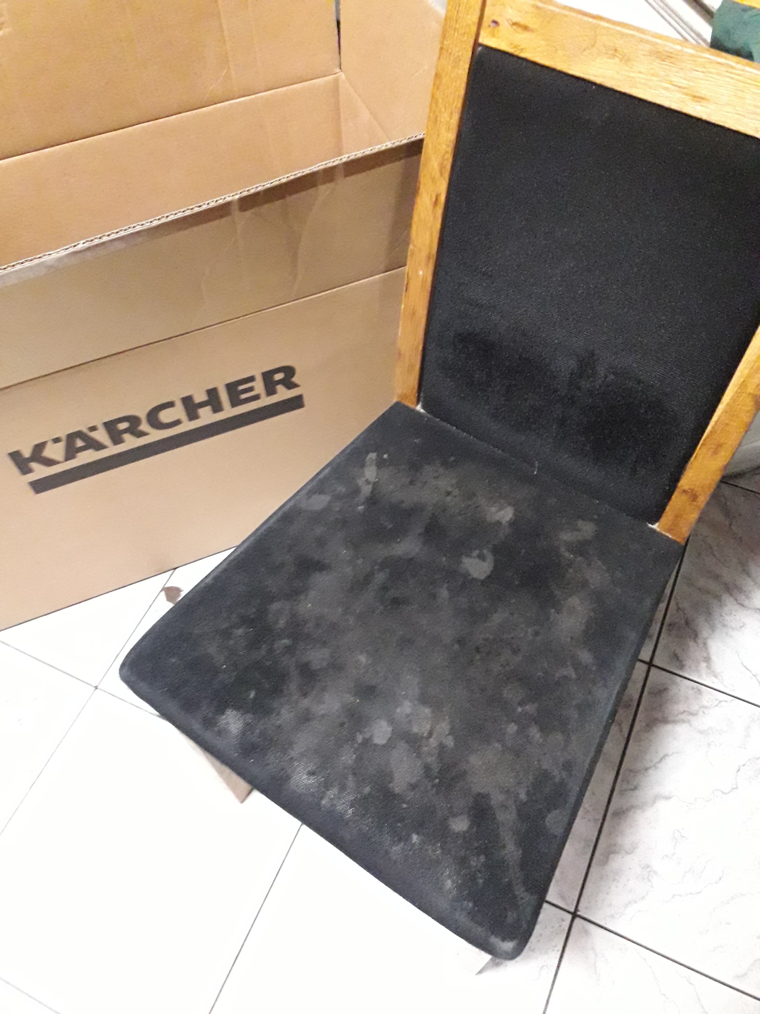 Tapicerowane krzesło z widocznymi plamami na siedzisku, obok karton z logo Kärcher, sugerujący użycie sprzętu tej firmy do czyszczenia tapicerki.