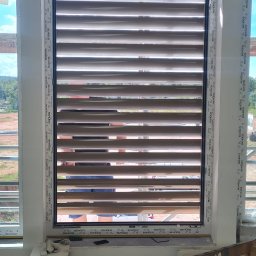 DUET SPÓŁKA Z OGRANICZONĄ ODPOWIEDZIALNOŚCIĄ - Zamknięte, poziome żaluzje w oknie podczas montażu, widoczna drabina i materiały budowlane w surowym wnętrzu.