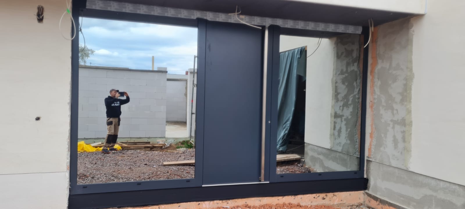 Nowoczesne, grafitowe drzwi przesuwne zamontowane w surowym stanie budynku, z widocznym odbiciem osoby robiącej zdjęcie.