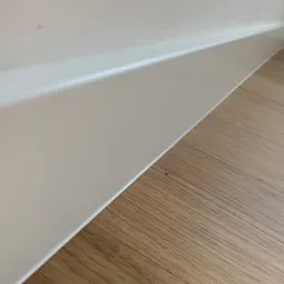 Szczegółowe ujęcie nowo położonej podłogi z paneli drewnianych i białej listwy przypodłogowej.