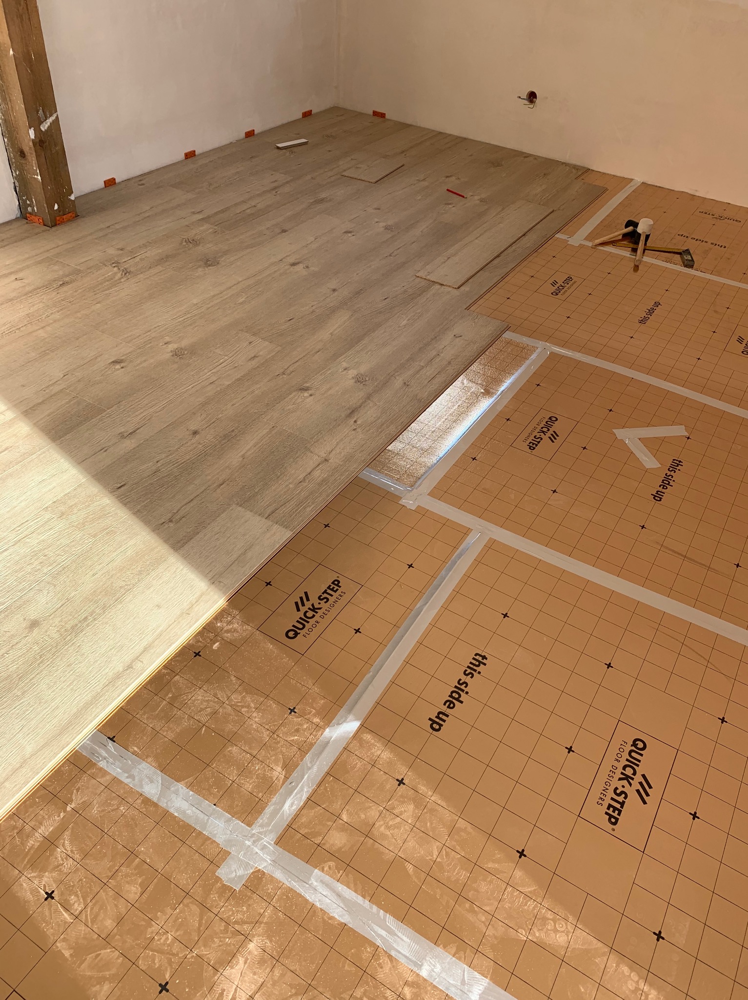 Fragment układania paneli podłogowych Quick-Step na podkładzie izolacyjnym, widoczne narzędzia i elementy montażowe.