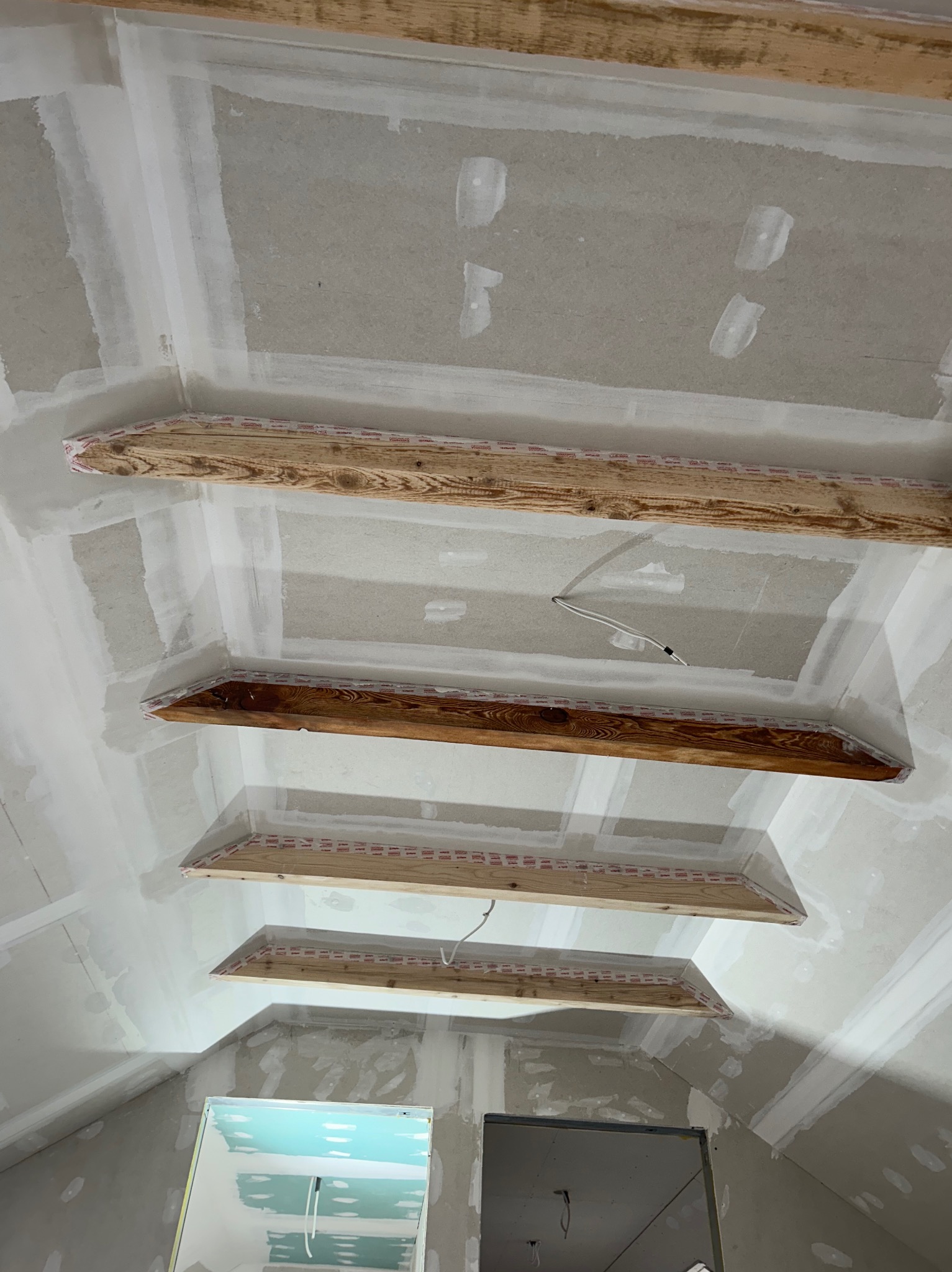 Sufit poddasza z drewnianymi belkami, płyty gipsowo-kartonowe w trakcie szpachlowania, widoczne kable elektryczne, przygotowanie do malowania.