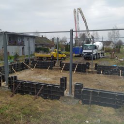 TAKIN USŁUGI BUDOWLANE DAWID JASKÓŁKA - Budowa fundamentów domu jednorodzinnego: szalunki systemowe, stalowe słupy, betonowóz z pompą, wywrotka w tle, pochmurny dzień.
