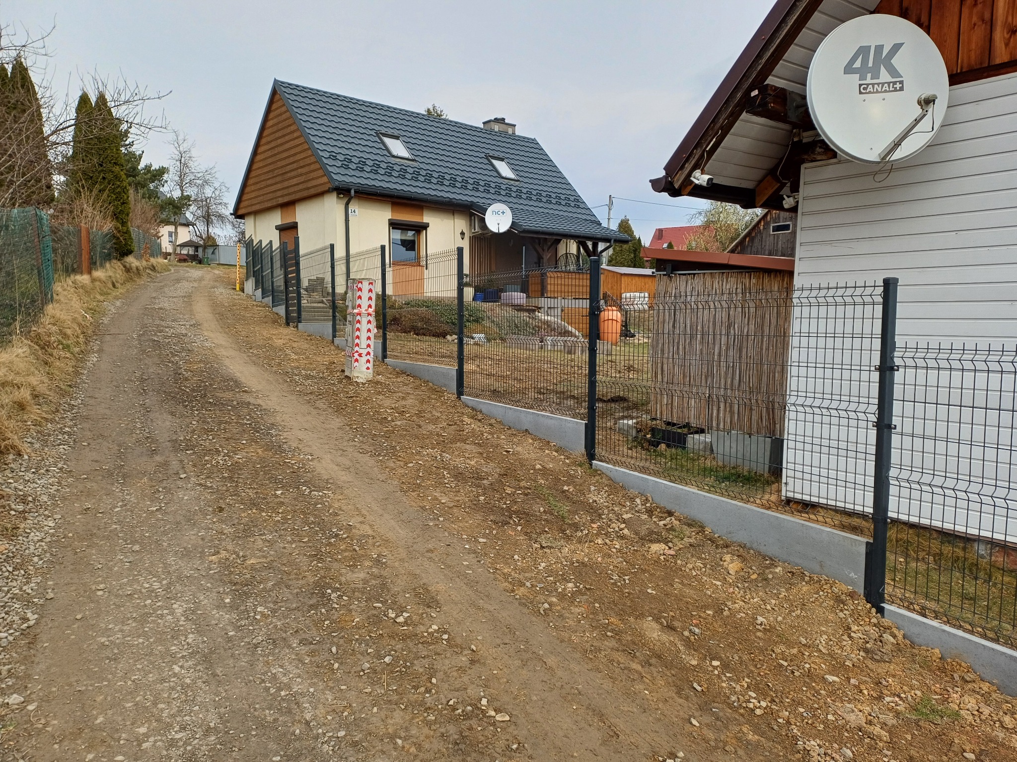 Nowoczesne ogrodzenie panelowe z podmurówką w Żywcu, widoczne na tle drogi gruntowej i domów jednorodzinnych. Słupki w kolorze grafitowym.