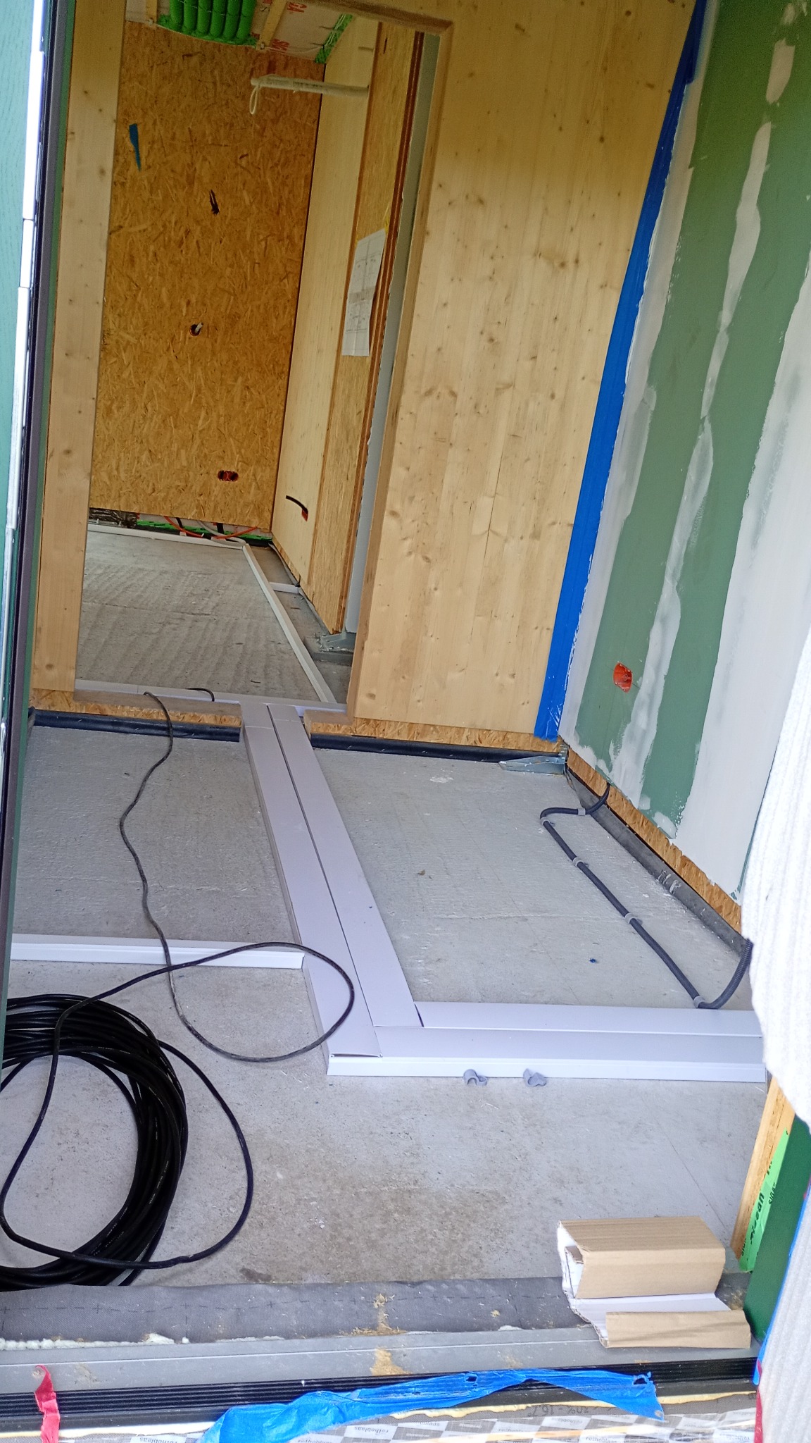 Wnętrze w trakcie budowy: widoczne kable elektryczne ułożone wzdłuż ściany, drewniane elementy konstrukcyjne i płyty gipsowo-kartonowe. Etap prac instalacyjnych.