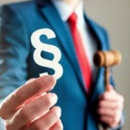 KANCELARIA AD REM IRENEUSZ KURT - Mężczyzna w niebieskim garniturze i czerwonym krawacie trzyma w dłoni biały symbol paragrafu, a w drugiej ręce drewniany młotek sędziowski.