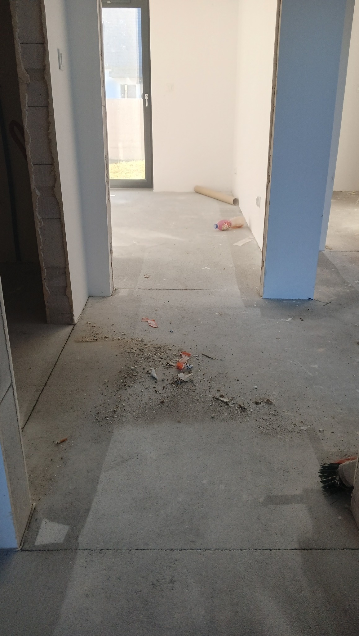 Surowy beton w nowym wnętrzu z gruzem i resztkami po budowie. Widoczne ślady po pracach wykończeniowych, przygotowanie do sprzątania pobudowlanego.