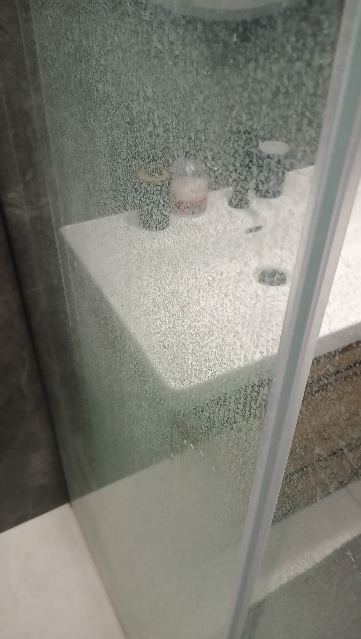 Szklana kabina prysznicowa pokryta osadem z mydła i kamienia, widok z bliska na zanieczyszczoną powierzchnię, armatura łazienkowa w tle.