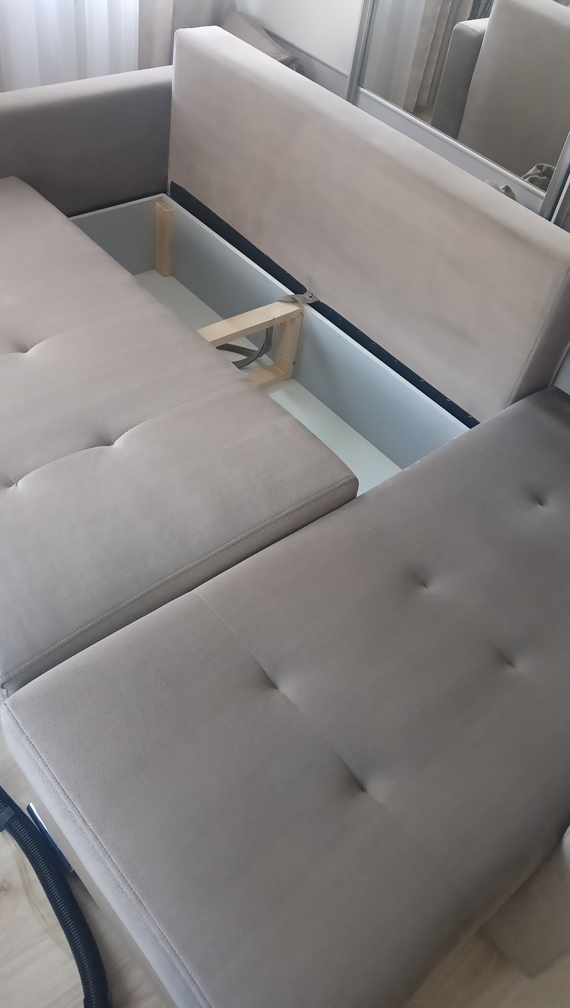 Jasna, rozłożona kanapa z widocznym pojemnikiem na pościel. Widoczny fragment węża odkurzacza sugeruje usługę prania tapicerki.