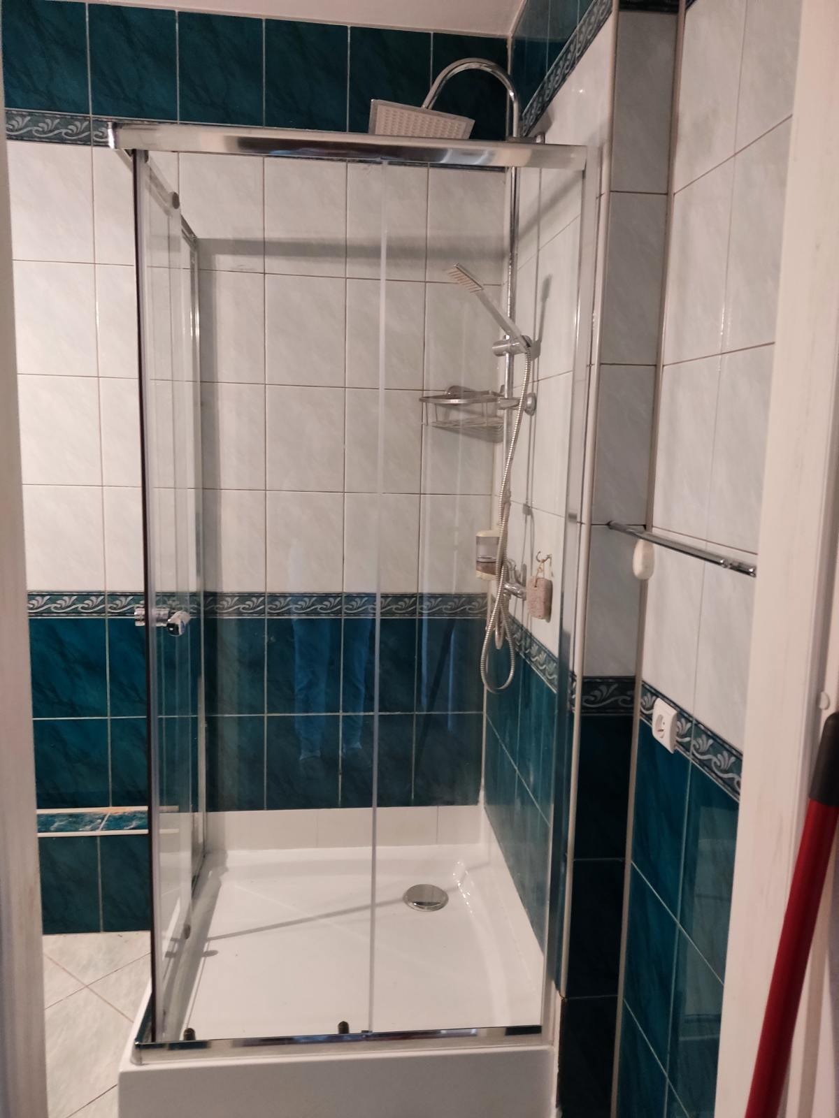 Nowoczesna kabina prysznicowa z chromowanymi profilami i szklanymi drzwiami, zainstalowana w łazience z białymi i turkusowymi płytkami ceramicznymi z dekoracyjnym wzorem.