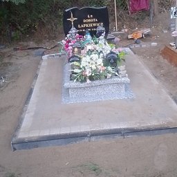 Spec-Kop Patryk Zalewski - Granitowy nagrobek z kwiatami i zniczami na cmentarzu, otoczony piaskiem i kostką brukową, widoczna butelka po napoju