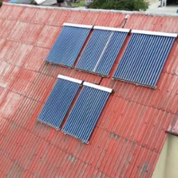 Rdzawa blacha falista dachu z zamontowanymi czterema panelami solarnymi z rur próżniowych, widok z góry.