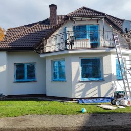 HYDROSERWIS-MALOWANIE, USZCZELNIANIE, CZYSZCZENIE, RENOWACJA DACHÓW, ELEWACJI, KOSTKI - Dom jednorodzinny z balkonem w trakcie przygotowań do malowania elewacji, okna zabezpieczone folią, widoczna drabina, agregat malarski i sprzęt. Zabezpieczony teren wokół budynku.