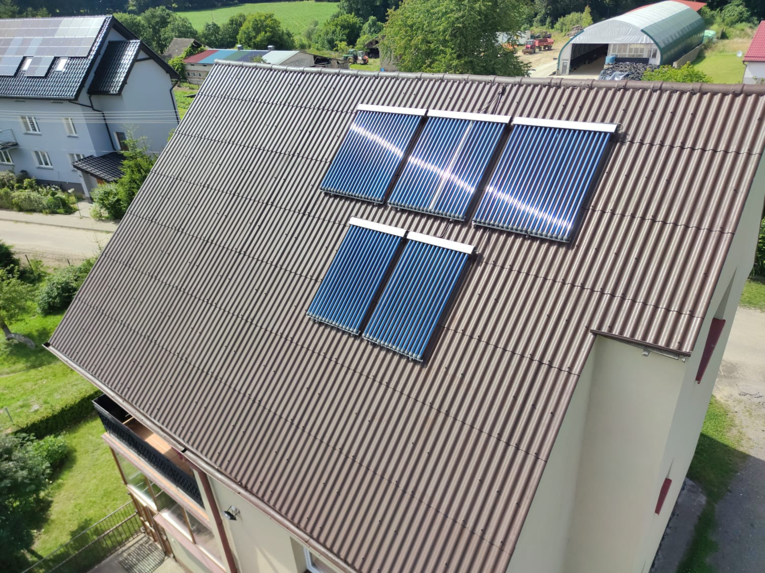 Brązowy dach z blachy falistej z zamontowanymi czterema panelami solarnymi, widok z góry na dom i okolicę.