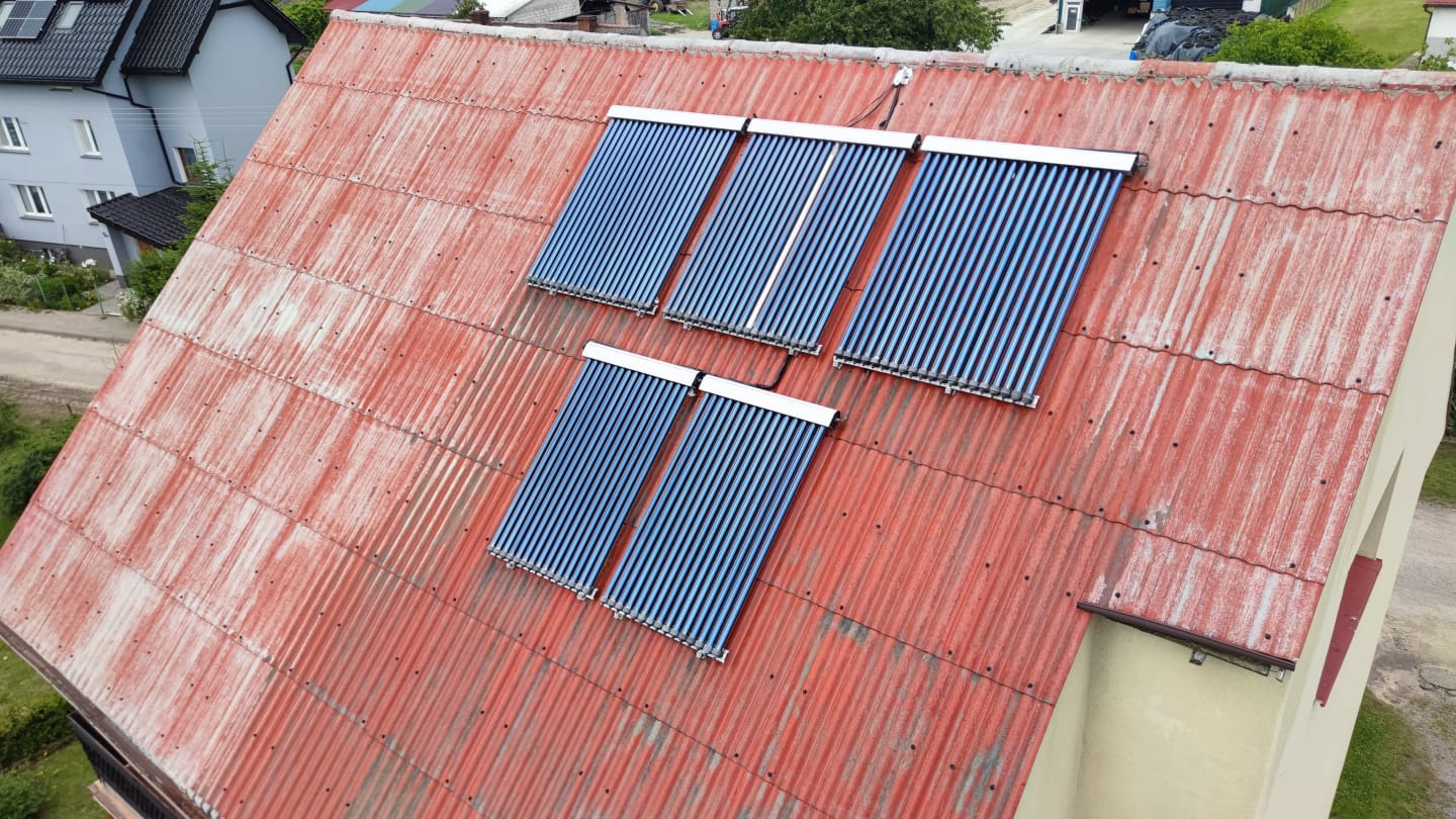 Rdzawa blacha falista dachu z zamontowanymi czterema panelami solarnymi z rur próżniowych, widok z góry.