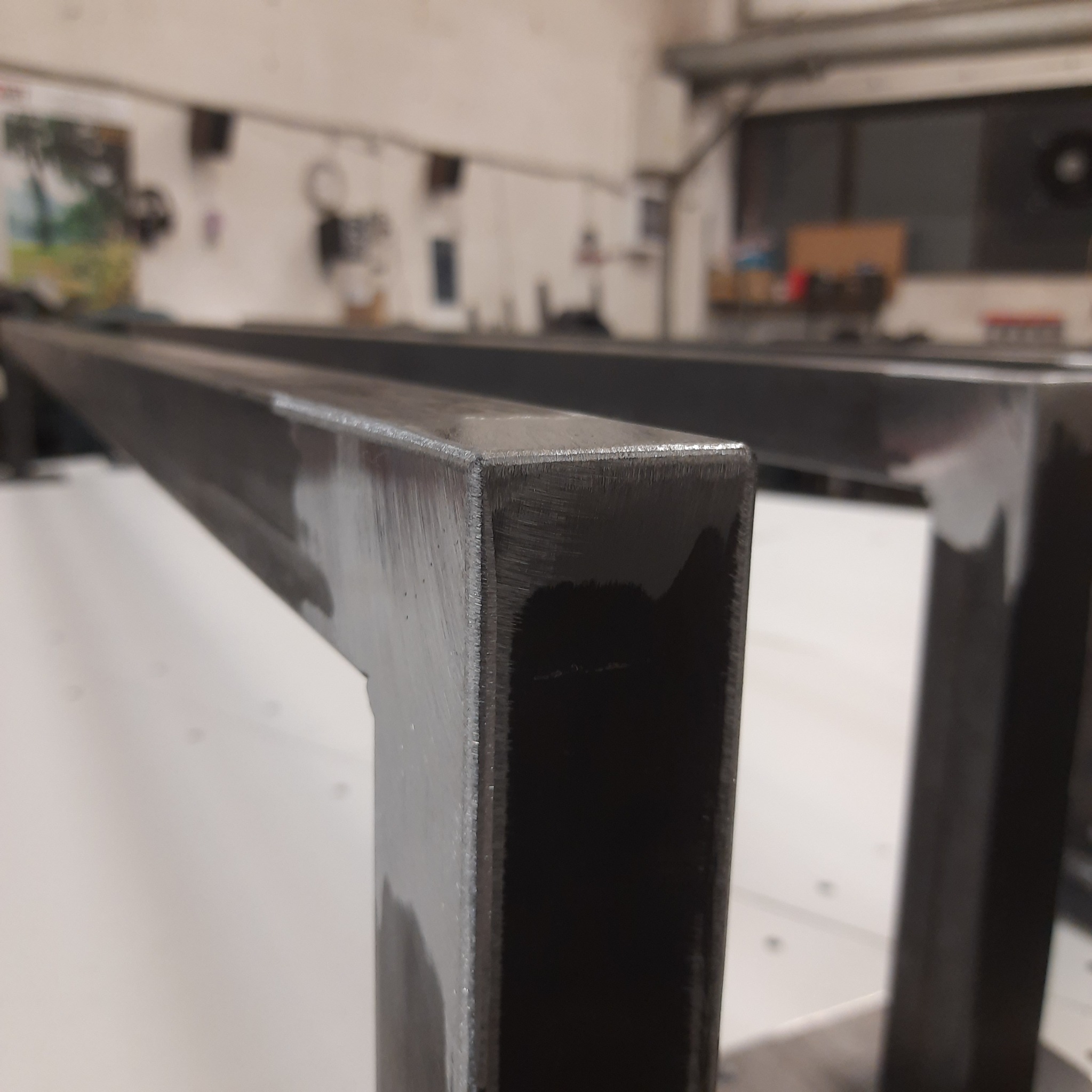 Szczegółowy widok spawanej, czarnej, metalowej konstrukcji z profili zamkniętych, z widocznymi śladami obróbki, na tle warsztatu.