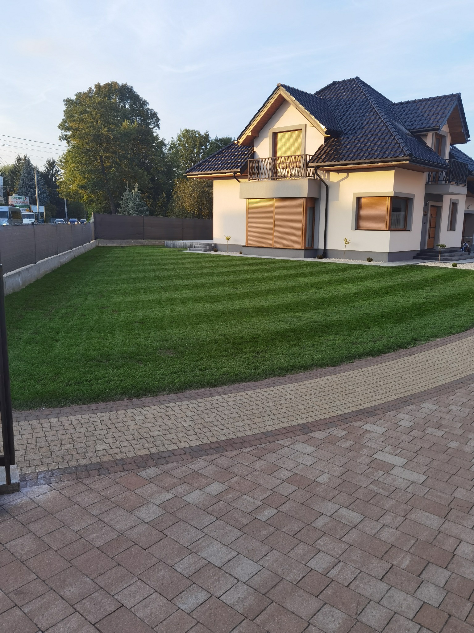 Perfekcyjnie przystrzyżony trawnik z wyraźnymi pasami przed nowoczesnym domem z balkonem, widok z poziomu kostki brukowej.