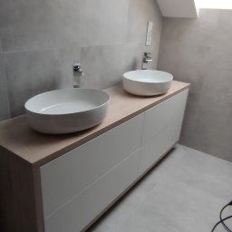 SZYMAŁA TARSYCJUSZ - Nowoczesna łazienka z dwiema okrągłymi umywalkami nablatowymi i szafką z białymi frontami, oświetlona światłem z okna dachowego. Minimalistyczny design.