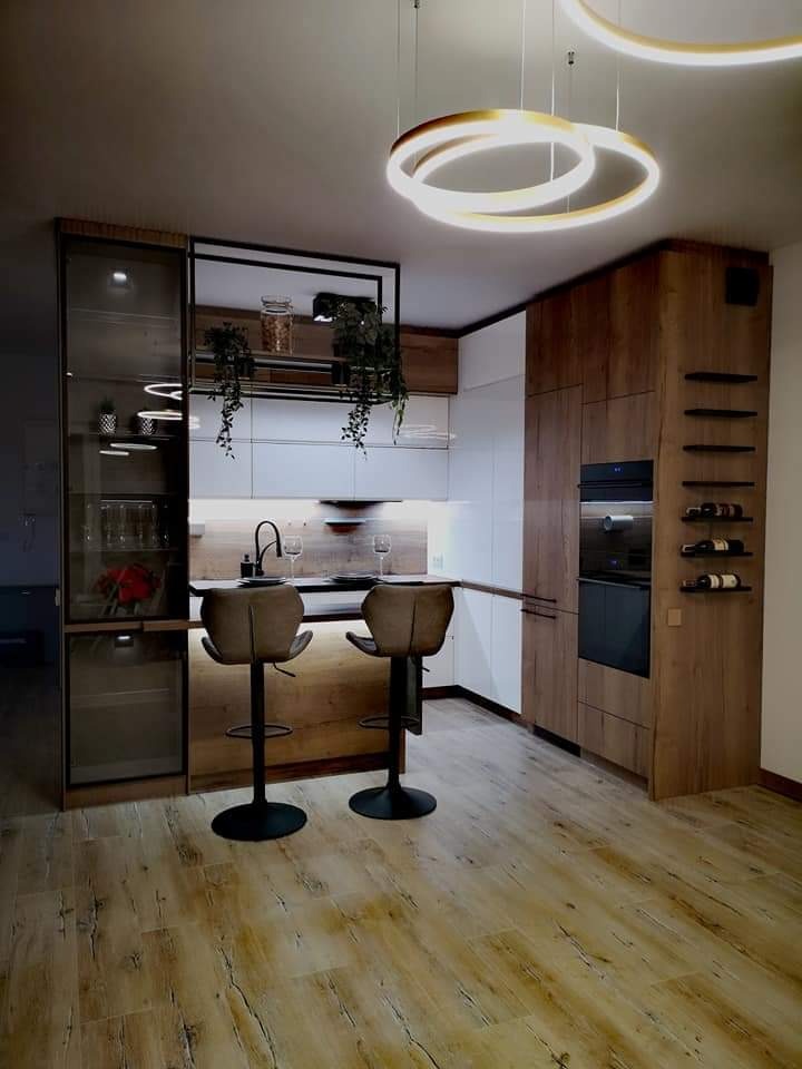Nowoczesna kuchnia z drewnianymi akcentami, wyspą z hokerami i oświetleniem LED. Szklana witryna z dekoracjami i półki na wino dodają elegancji.