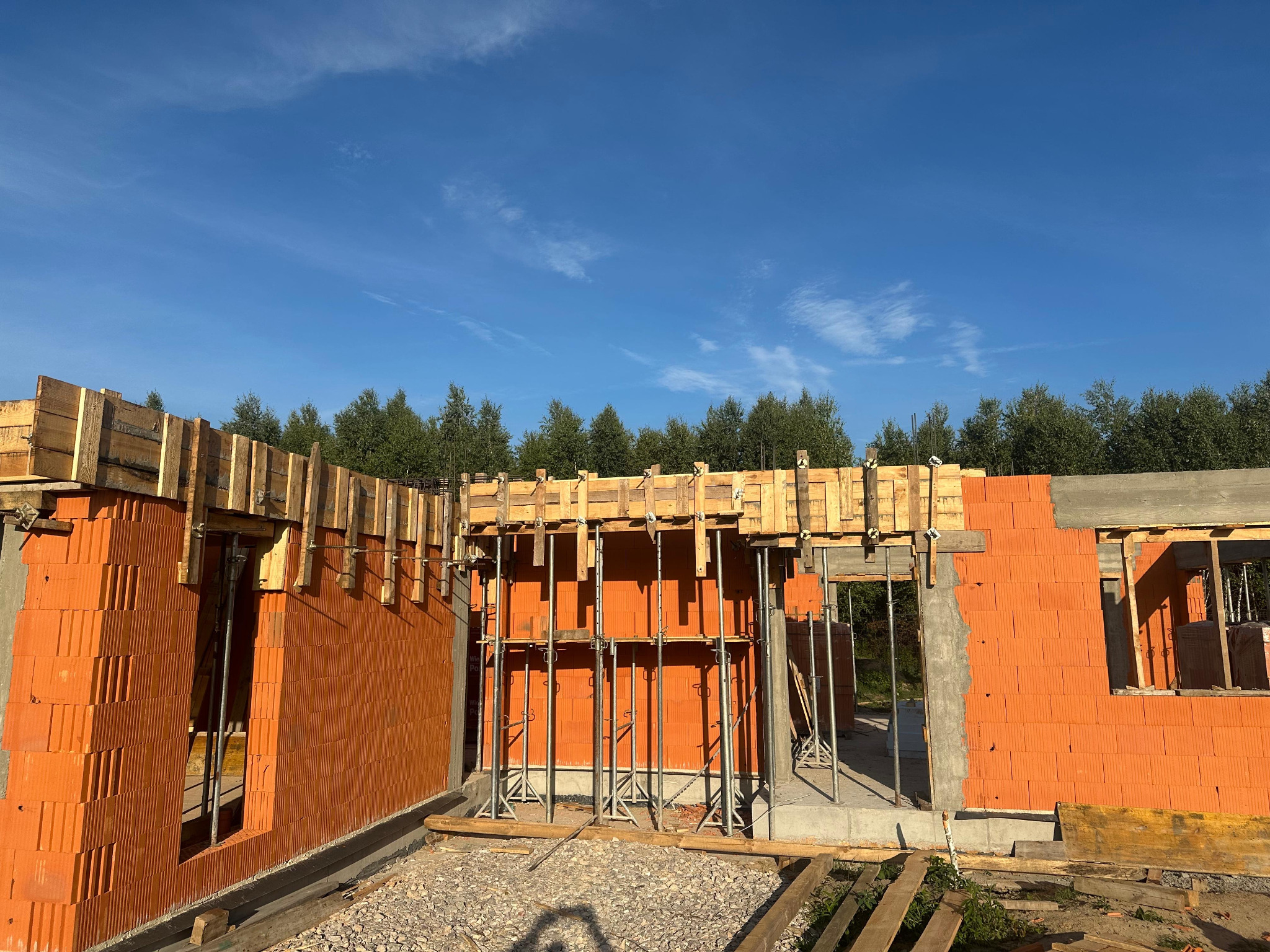 Wznoszenie ścian z pustaków ceramicznych Porotherm, z widocznym szalunkiem i podporami. Budowa domu w trakcie realizacji, błękitne niebo w tle.