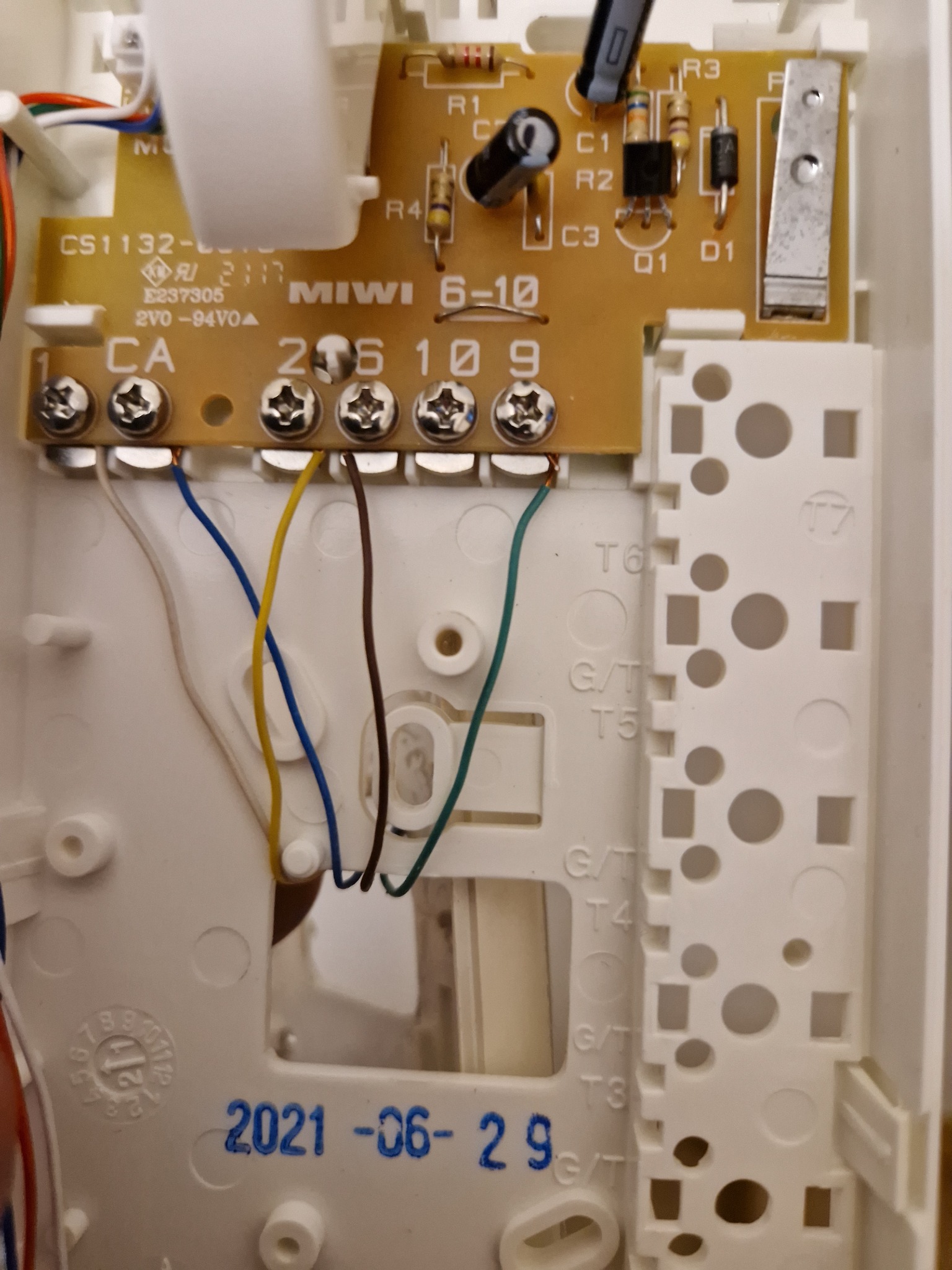 Wnętrze obudowy domofonu MIWI 6-10 z widoczną płytką drukowaną, elementami elektronicznymi, listwą zaciskową z podłączonymi przewodami w kolorach: białym, niebieskim, żółtym, brązowym i zielonym...