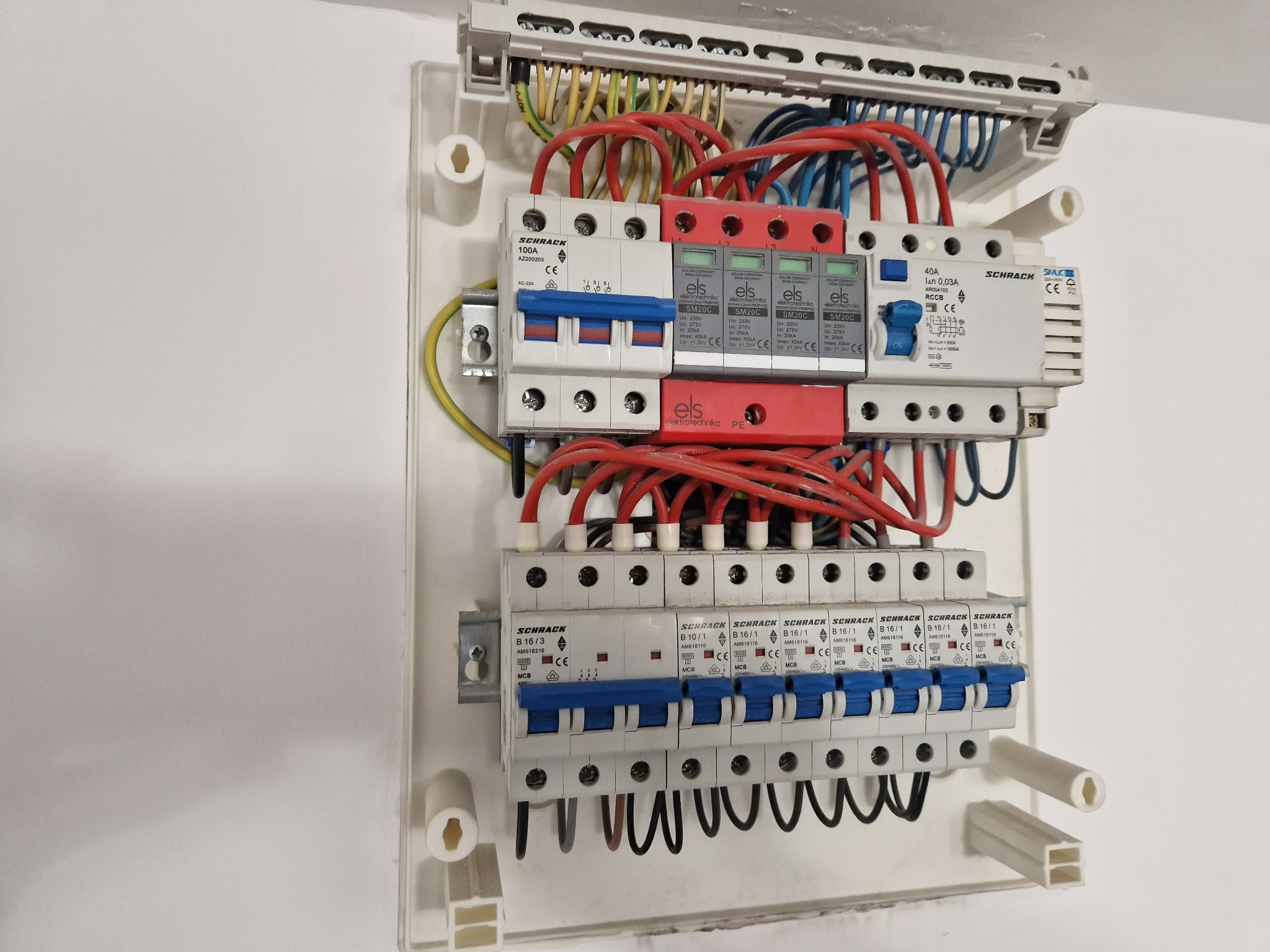Rozdzielnica elektryczna Schrack z zabezpieczeniami ELS, widoczne przewody w kolorach czerwonym, żółtym i niebieskim, zamontowana na białej ścianie.