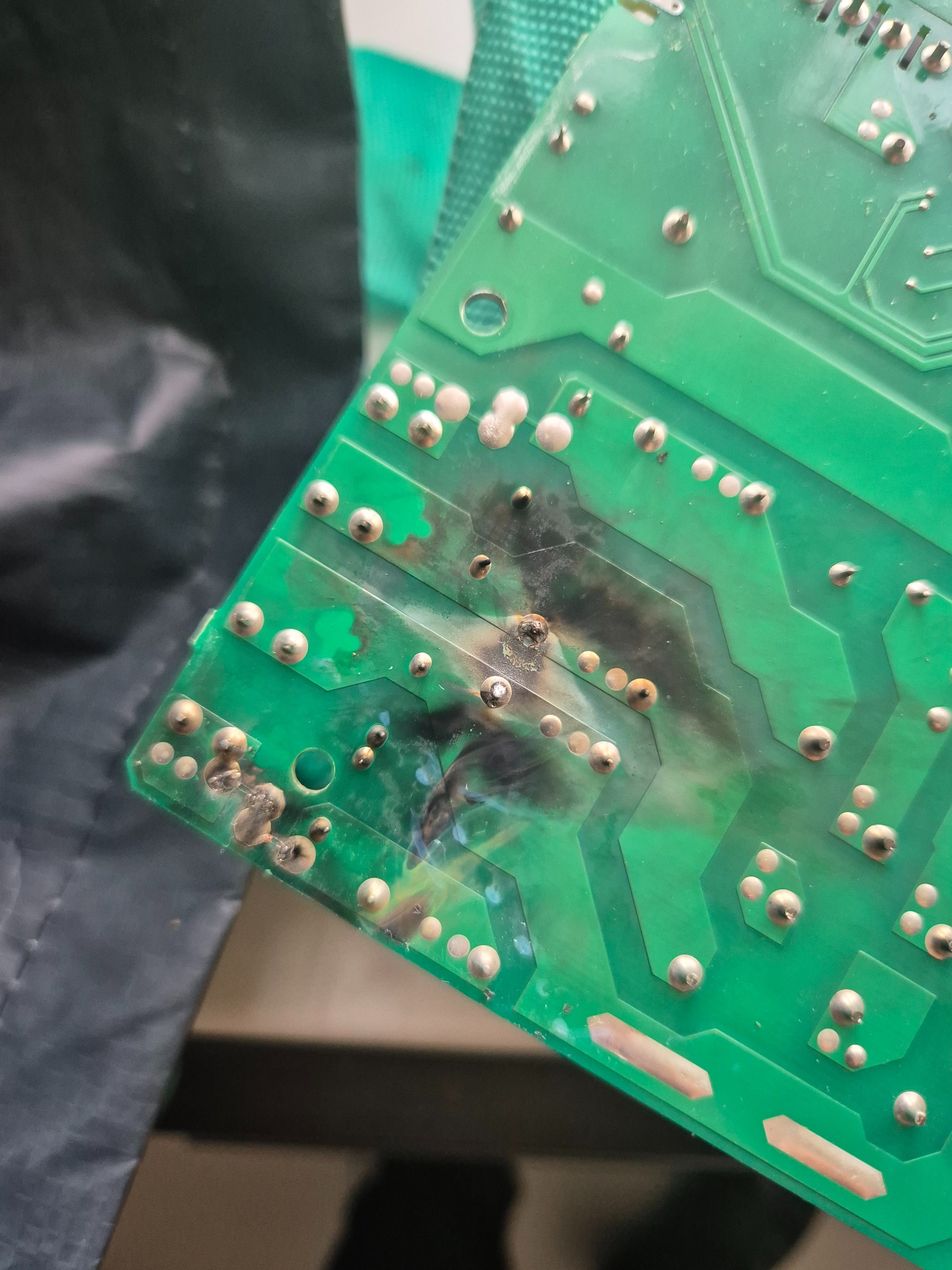 Uszkodzona, zielona płytka drukowana z widocznymi śladami przepalenia i nadpalonymi elementami lutowanymi.