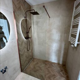 Jarosław Rudnicki Remontovo 3City - Nowoczesna łazienka z kabiną prysznicową typu walk-in, wykończona beżowymi płytkami w dwóch odcieniach i wzorach, z deszczownicą w kolorze miedzi oraz okrągłym lustrem z podświetleniem LED.