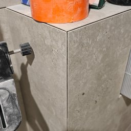 Technika Budowlana Konrad Kołecki - Wykończony narożnik obłożony szarymi płytkami w Lutomiersku, widoczne akcesoria glazurnicze: taśma malarska Grohe, poziomica i drobne narzędzia.