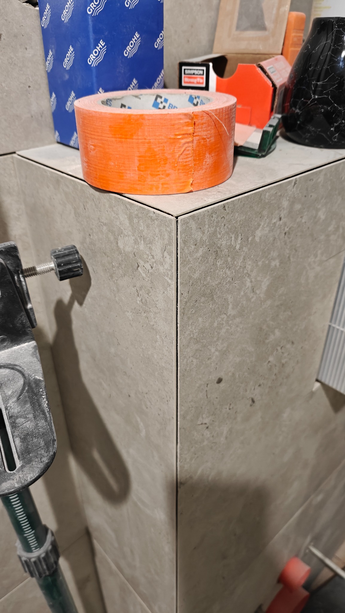 Wykończony narożnik obłożony szarymi płytkami w Lutomiersku, widoczne akcesoria glazurnicze: taśma malarska Grohe, poziomica i drobne narzędzia.