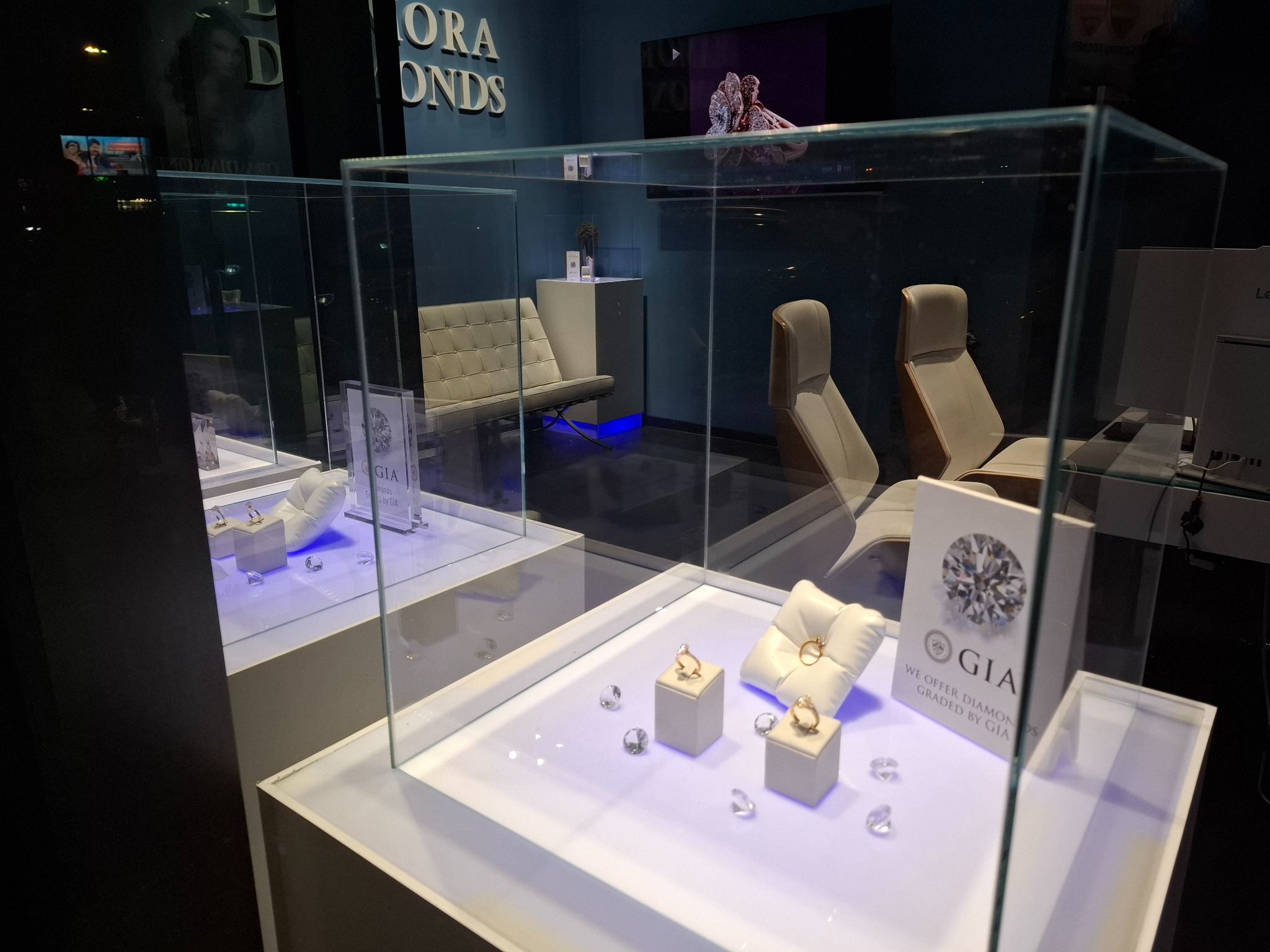 Ekskluzywny salon jubilerski z złotymi pierścionkami i diamentami w szklanych gablotach, oświetlonych subtelnym, niebieskawym światłem, z minimalistycznym wystrojem i logo GIA.
