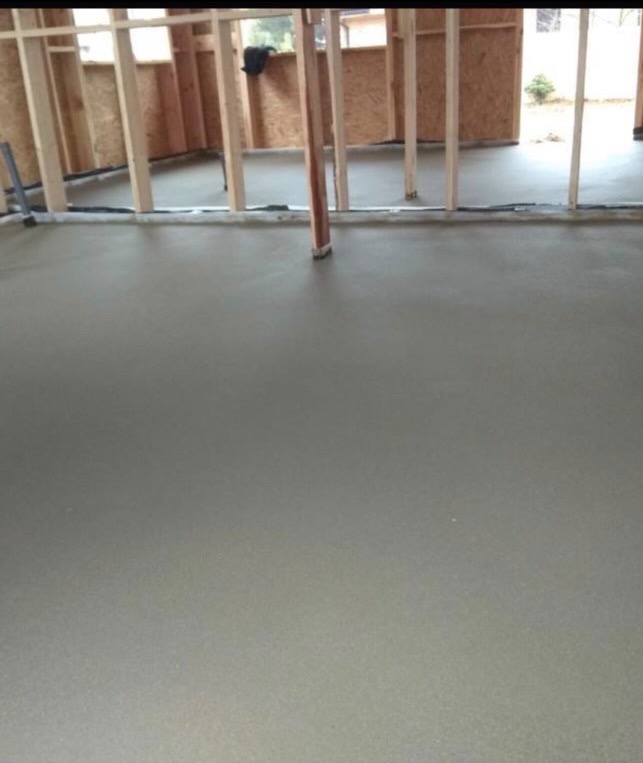 Świeżo wylana, gładka posadzka w surowym stanie, widoczne drewniane elementy konstrukcyjne ścian i podłoże przygotowane pod dalsze prace wykończeniowe.