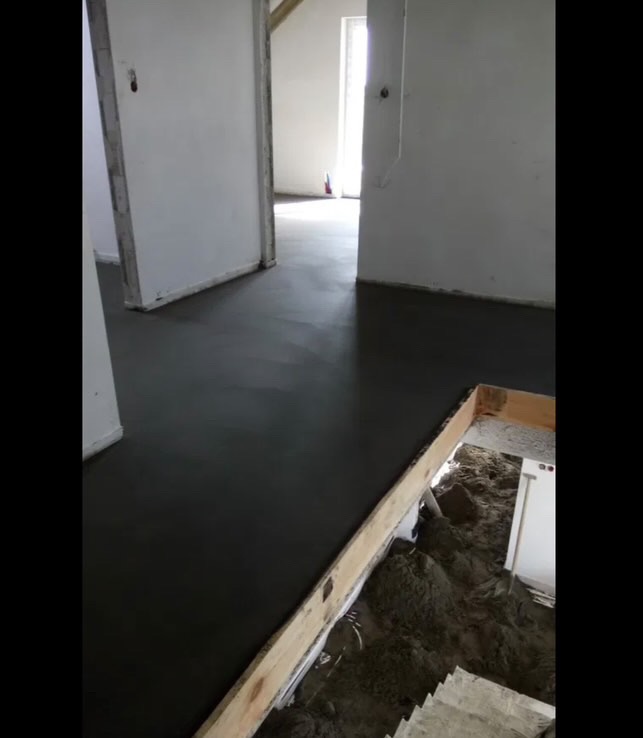 Świeżo wylana, gładka wylewka podłogowa w surowym wnętrzu z widocznymi ościeżnicami i przygotowanym materiałem do dalszych prac.