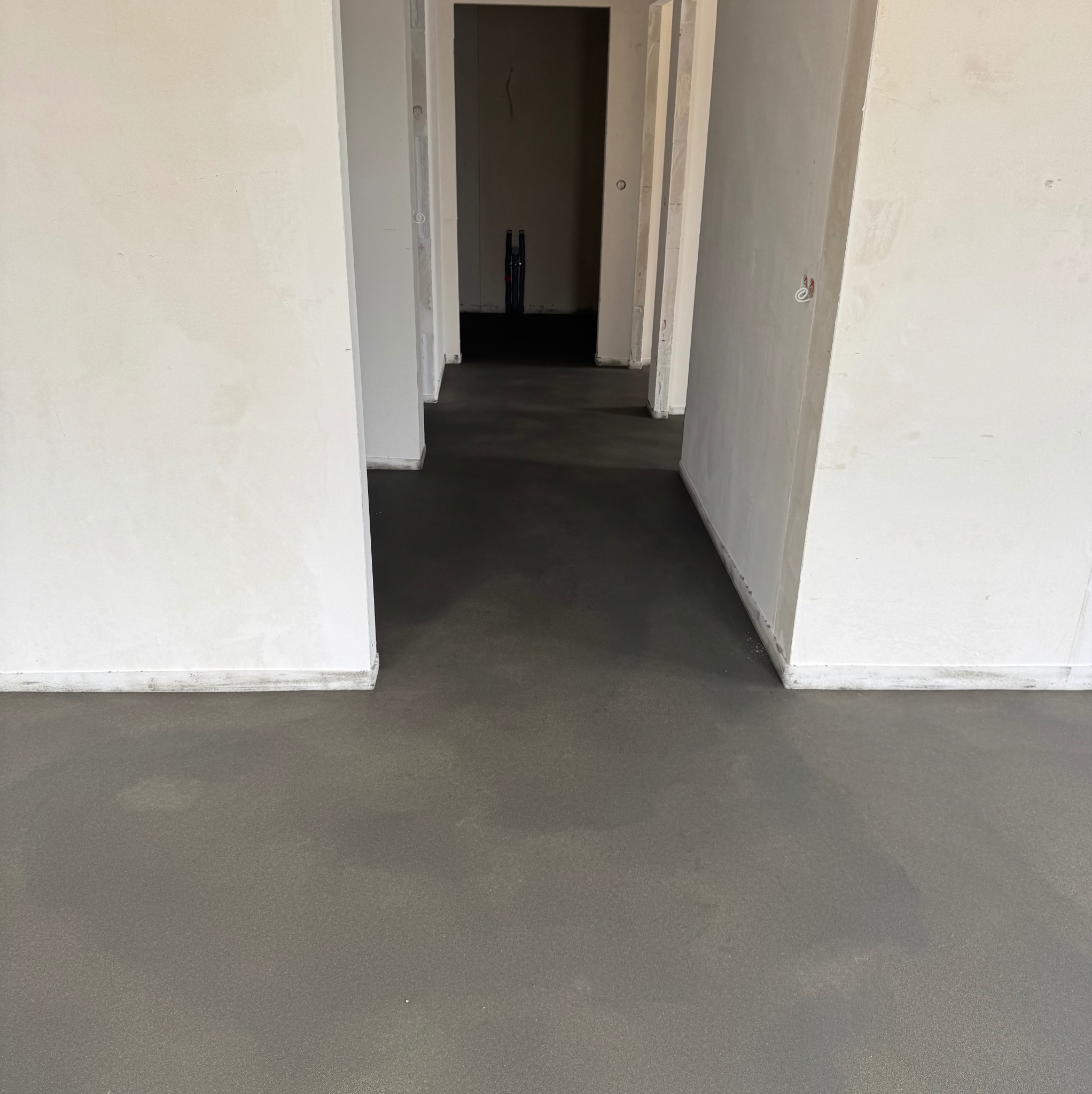 Świeżo wylana, gładka posadzka jastrychowa w jasnym wnętrzu z widocznymi otworami drzwiowymi. Szara, jednolita powierzchnia podłogi.