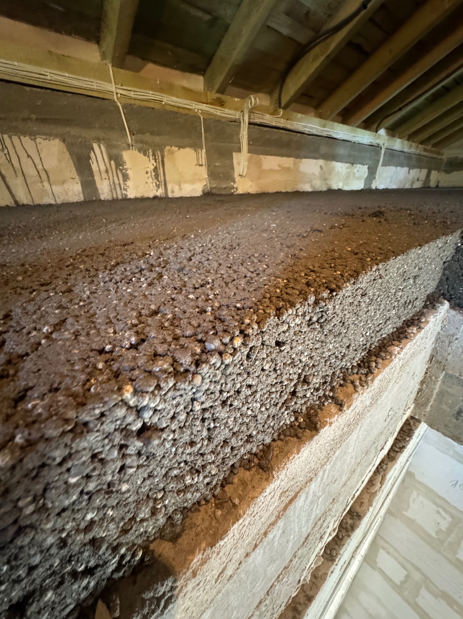 Surowa, szara posadzka jastrychowa z widoczną strukturą kruszywa, ułożona na nierównej powierzchni. W tle drewniany strop i instalacje elektryczne.